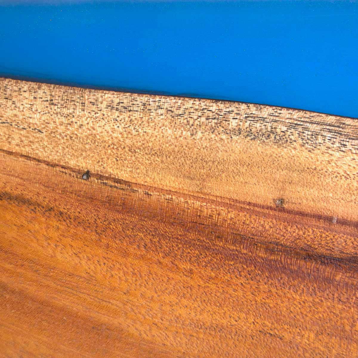 Live edge Cuban Mahogany wood with translucent bright blue epoxy resin, a detailed close up image to show the natural wood grain