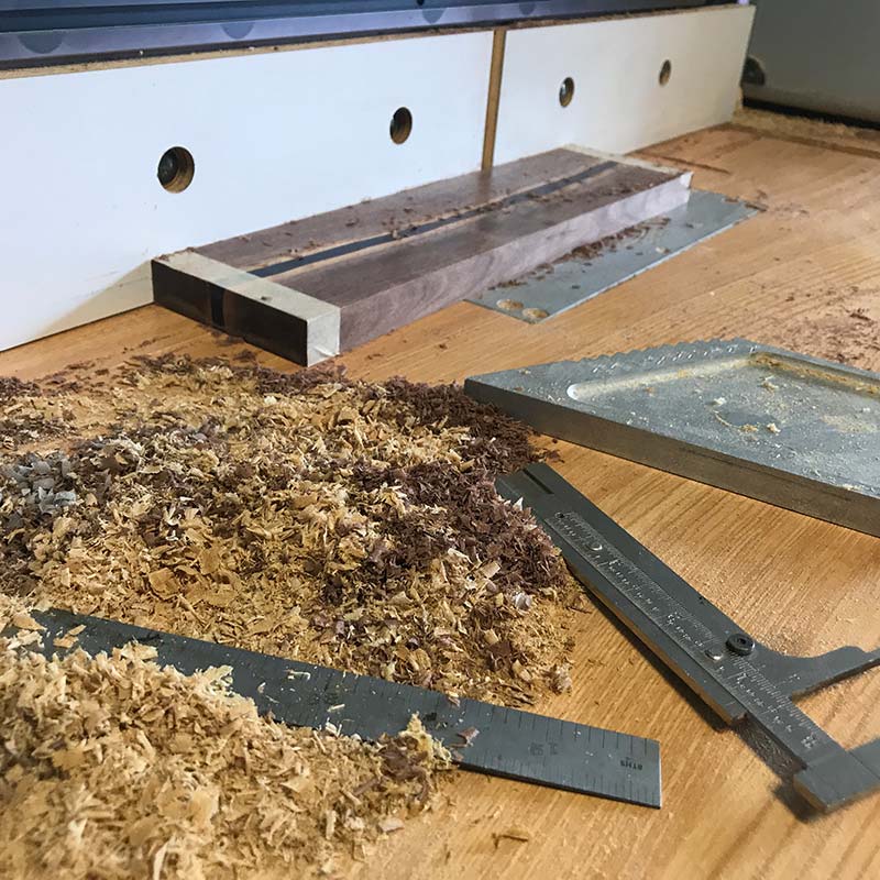 calipers and ruler on a router table while routing channels for hidden magnets in a walnut and blue epoxy resin magnetic knife holder