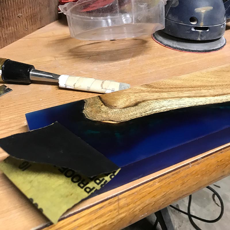 hand sanding with sandpaper a blue epoxy resin and salvaged wood magnetic knife holder