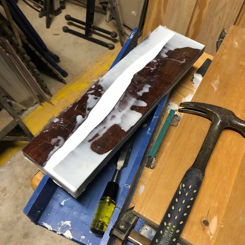using a hammer and chisel to remove a live edge epoxy resin magnetic knife holder from a plastic reusable epoxy resin form