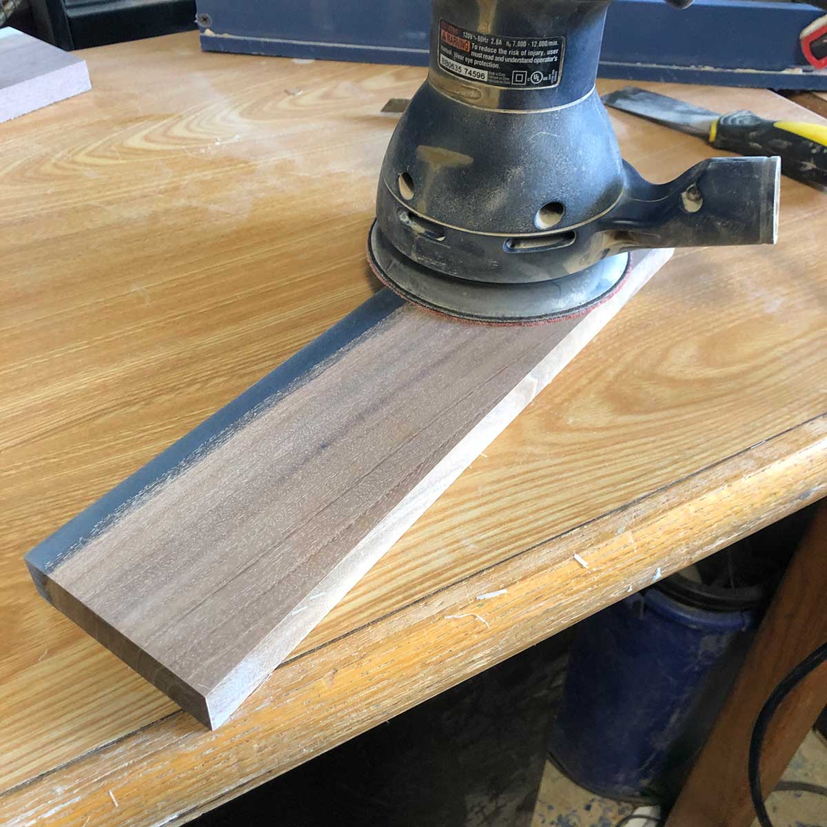 using an orbital palm sander to sand a wood and epoxy magnetic knife holder made from salvaged lumber and epoxy resin