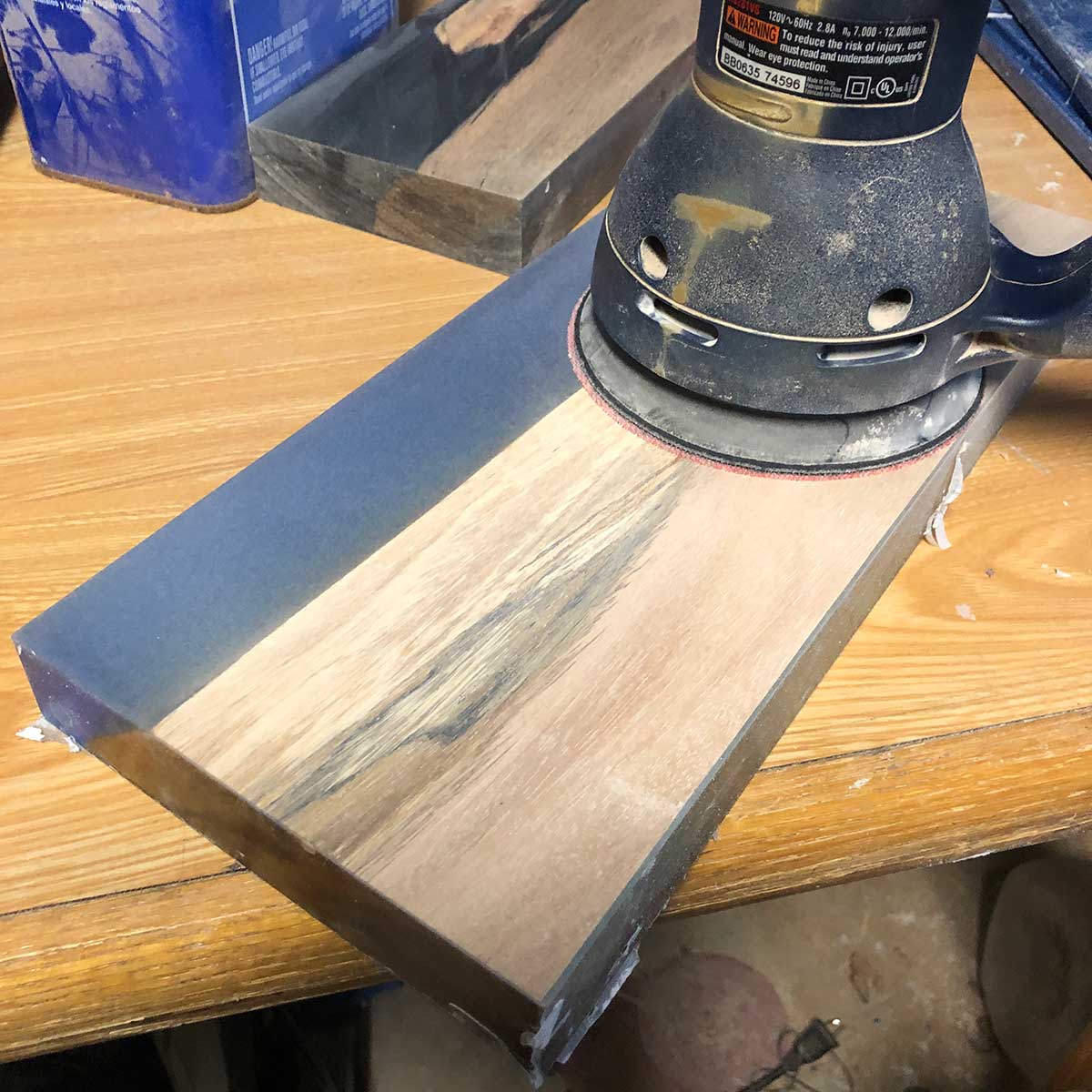 using an orbital sander to sand a knife rack made from salvaged acacia wood and blue epoxy resin